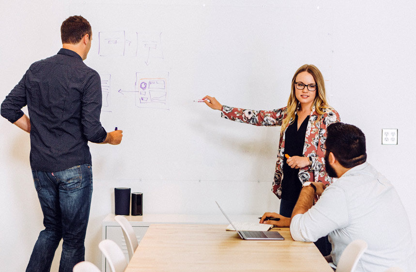 Woman pointing at a whiteboard in front of a sitting man